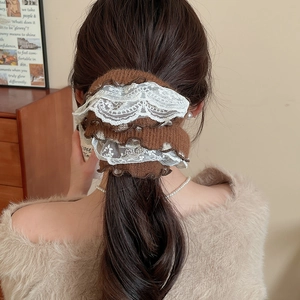 Detailed view of a brown knitted scrunchie with white lace trim on a low ponytail