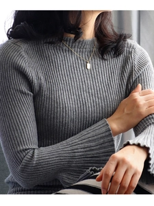 Close-up of gold rectangular letter pendant necklace worn with grey ribbed knit sweater