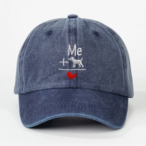 Detail of embroidered Me dog heart design on a washed denim baseball cap in dark blue