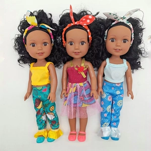 Three realistic African baby dolls with curly hair wearing colorful outfits on white background