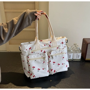 Detail of white tote bag with red cherry print featuring external zipper pockets