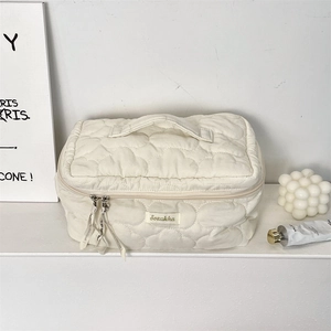 Close-up of a white quilted cloud makeup bag featuring a top handle and decorative ribbon