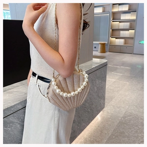 Beige shell-shaped bag with pearl handle and gold chain worn by a model in a modern lobby