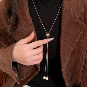 Détail d'un collier lasso doré avec perles blanches porté sur un vêtement en velours côtelé