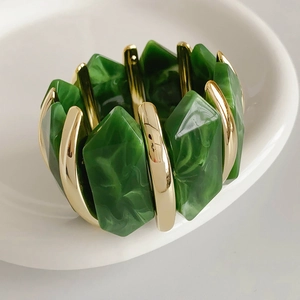 Détail du bracelet en résine marbrée verte avec touches dorées sur plat blanc