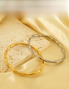 Detail of gold and silver bamboo shaped stainless steel bangles on beige stone