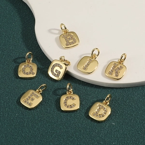 Golden square alphabet pendants with cubic zirconia inlay on a textured dark background