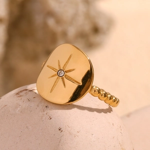 Macro detail of 18K gold-plated starburst ring with zircon on textured stone surface