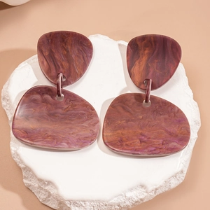 Macro detail of irregular resin earrings featuring marbled texture and geometric shapes