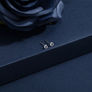 Macro shot of silver heart studs with S925 hallmark detail on dark rose background