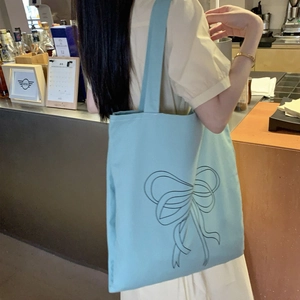 Lifestyle-Foto der hellblauen Canvas-Tasche mit schwarzem Bogendruck an der Schulter