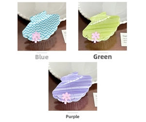 Detail view of shell-shaped acetate hair claws with floral accents in blue, green, and purple