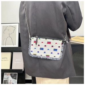 Detail of denim crossbody bag featuring colorful geometric patches and silver chain strap