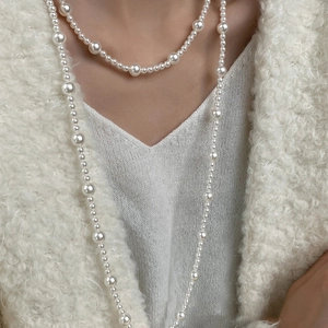 Long faux pearl necklace with geometric layers worn over a cozy white knit sweater