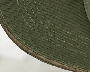 Détail des coutures renforcées sur la visière courbée d'une casquette vert foncé