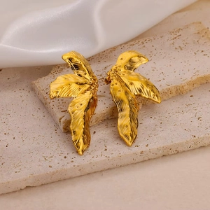 Macro shot of gold-plated wing earrings with detailed leaf texture on travertine stone