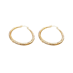 Boucles d'oreilles créoles dorées avec texture géométrique sur un fond blanc épuré