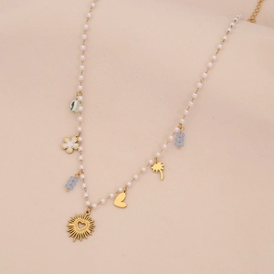 Détail d'un collier doré avec perles et pendentifs cœur, palmier et soleil sur tissu