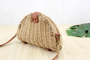 Detailed close-up of semi-circular straw crossbody bag with brown leather strap and rivets