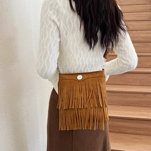 Brown suede crossbody bag with layered fringe and silver snap button on wooden stairs