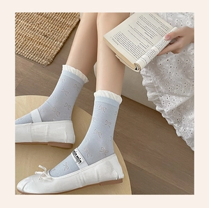 Close-up of light blue cotton crew socks with white bow prints and ruffled trim details