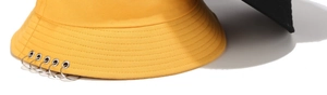 Détail du chapeau bob en coton jaune avec cinq anneaux métalliques sur le bord