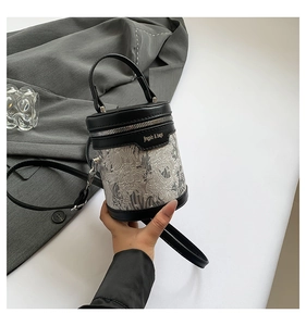 Detailed close-up of a black cylinder bucket bag with grey oriental embroidery and gold logo