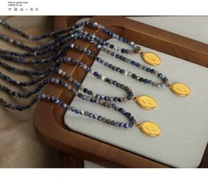 Detail of four handmade beaded necklaces with gold oval religious pendants on a wooden tray
