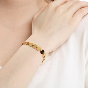 Close-up of a polished gold disc chain bracelet worn on a wrist for a modern look