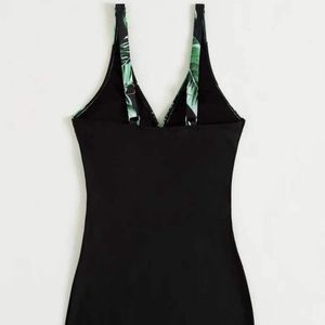Black one-piece swimsuit featuring green tropical leaf print straps with adjustable buckles