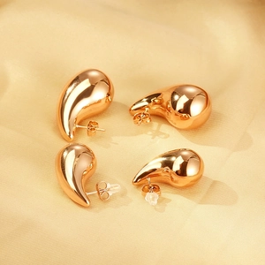Detailed view of glossy golden teardrop earrings on soft beige satin fabric background