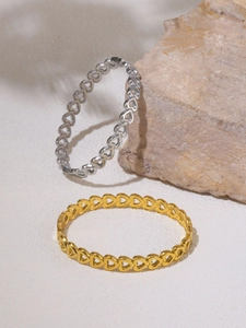 Detailed view of hollow heart pattern bangles in gold and silver finish on sand