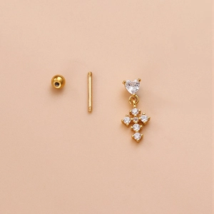 Macro detail of gold cross and heart earring with zircon stones on soft pink background