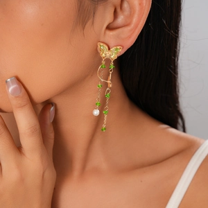 Detail of a gold butterfly earring with green stones and pearl on a model