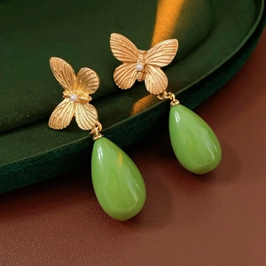 Détail de boucles d'oreilles papillon dorées avec perles et pendentifs goutte d'eau verts