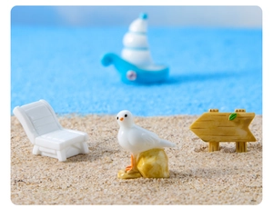 Miniature beach scene set with white deck chair, seagull on rock, and wooden signpost
