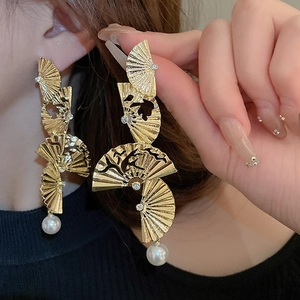 Detail of gold fan-shaped tassel earrings with pearls and crystals on a female model