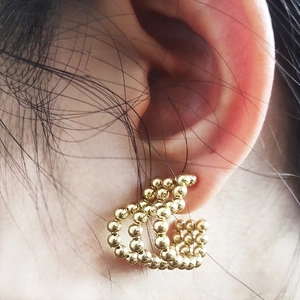 Close-up of a golden C-shaped earring featuring heart and bead charms worn on the ear