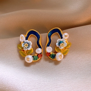 Detailed close-up of vintage enamel floral earrings with pearls on beige silk fabric