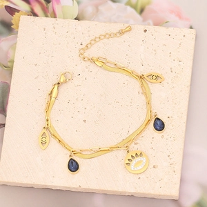 Pulsera dorada de varias capas con amuletos de ojo y piedras azules sobre piedra