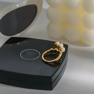 Elegant gold stainless steel ring featuring three white pearls on a black display surface