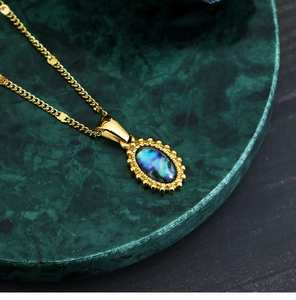 Detail of bohemian gold stainless steel oval pendant with blue abalone shell on marble