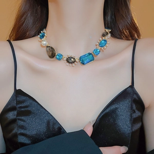 Close-up of golden necklace featuring blue and black gemstones with elegant pearl accents