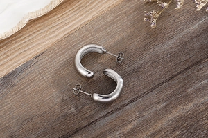 Detailed view of silver C-shaped hoop earrings on dark wood with a polished mirror finish