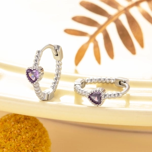 Silver heart earrings with purple crystals and beaded texture on warm background