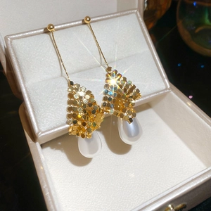 Macro detail of 18k gold plated drop earrings with white pearl and sparkling textures