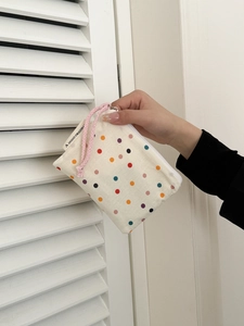 Close-up of beige canvas makeup bag with colorful polka dots and pink braided rope