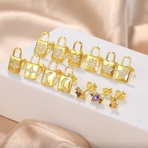 Detail of gold ear studs set with star and heart charms on satin background display