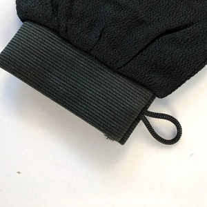 Close-up of black exfoliating glove featuring elastic wrist cuff and hanging loop detail