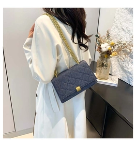 Detail of denim crossbody bag with quilted stitching and gold chain on white jacket